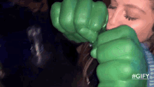 a woman wearing a green hulk glove is drinking from a cup