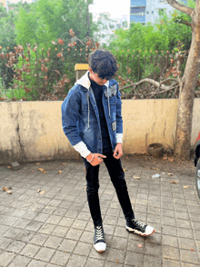 a young man wearing a denim jacket and black jeans is pointing at his pants