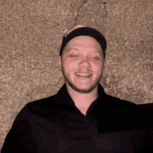 a man wearing a black shirt and a baseball cap smiles for the camera