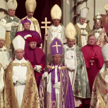 a group of priests are standing in a line with one wearing a purple robe with the letter t on it