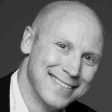 a black and white photo of a smiling bald man in a suit and tie .