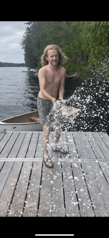 a shirtless man is standing on a dock spraying water at the camera