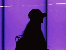 a silhouette of a woman wearing a hat and a backpack is standing in front of a purple wall .