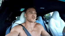 a shirtless man is sitting in the back seat of a car with a seat belt on .