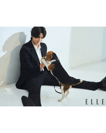 a man in a suit is playing with a dog and the word elle is on the bottom right