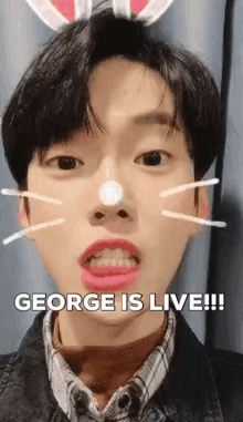 a young man with bunny ears on his head is making a funny face with the words `` george is live '' .