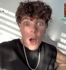 a young man with curly hair is wearing a black shirt and a silver chain around his neck