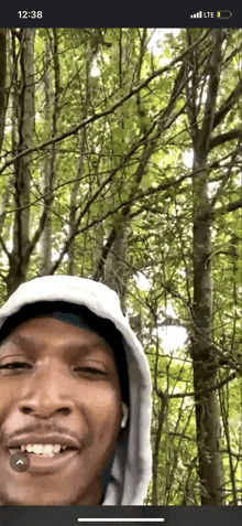 a man in a hooded sweatshirt is smiling in front of trees .