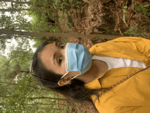 a woman wearing a yellow jacket and a blue face mask in the woods