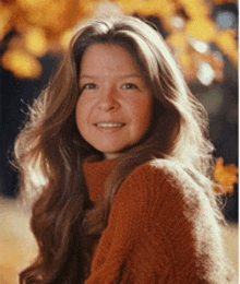 a woman with long brown hair is wearing an orange sweater and smiling