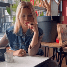 a woman in a denim vest sits at a table in front of a sign that says ' cafe '