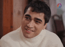 a young man wearing a white sweater is smiling .