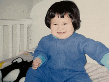 a baby in a blue outfit is sitting on a bed and smiling