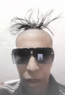 a man wearing sunglasses and a mohawk looks at the camera .