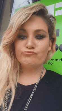 a woman making a funny face in front of a green sign that says joy