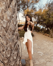 a woman in a white dress is leaning against a palm tree