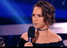 a woman wearing a choker is speaking into a microphone on a stage