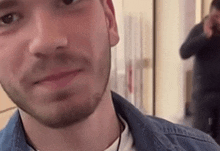 a close up of a man 's face with a beard and a denim jacket .