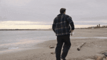 a man in a plaid shirt is walking along a beach