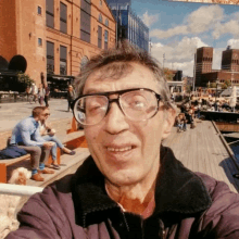 a man wearing glasses takes a selfie in front of a city