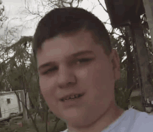 a young man in a white shirt is smiling for the camera while standing in front of a trailer .