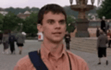 a man in an orange shirt is standing in front of a crowd of people in a park .