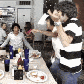 a man in a black and white striped shirt is standing in front of a table full of food and drinks