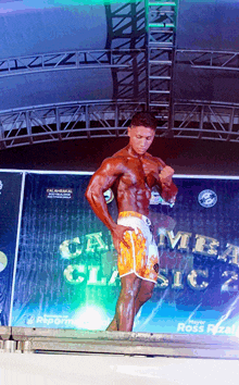 a bodybuilder stands on a stage in front of a banner that says carmel classic