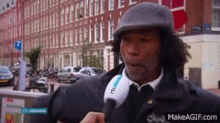 a man wearing a hat and tie is talking into a microphone on a street .