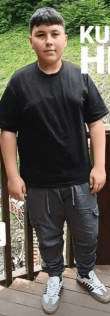 a boy wearing a black shirt and grey pants is standing on a balcony .