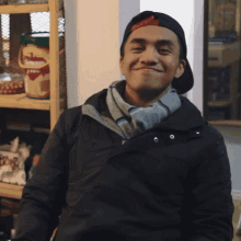 a man wearing a hat and a scarf smiles in front of a shelf with a bucket of beans on it