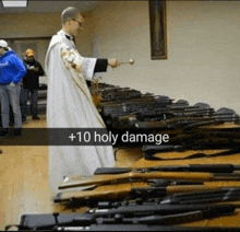 a priest is standing in front of a table full of guns with +10 holy damage written on the bottom of the photo