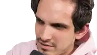 a man with a beard is wearing a pink hoodie and talking into a microphone