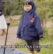 a little girl in a blue jacket is standing next to an umbrella with a caption in a foreign language