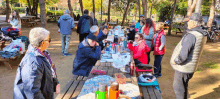 a group of people are gathered around a picnic table in the woods