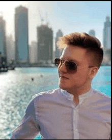 a young man wearing sunglasses is standing in front of a body of water .