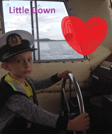 a little boy wearing a captain 's hat sits at the steering wheel of a boat