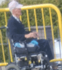 a man in a wheelchair is sitting in front of a yellow fence .