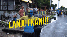 a man with blue and yellow paint on his face is standing next to a sign that says " lanjutkan "