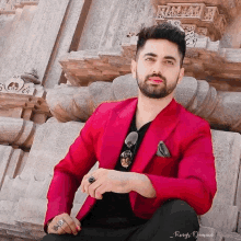 a man wearing a red jacket and black shirt is sitting in front of a stone wall