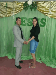 a man and a woman holding hands in front of a green curtain with the word jesus on it