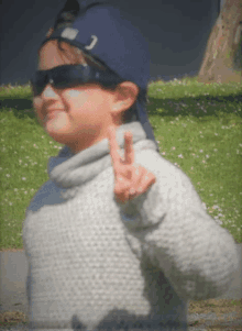 a young boy wearing sunglasses and a baseball cap is giving a peace sign