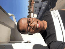 a man wearing glasses and a black guess shirt smiles for the camera