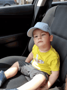 a young boy wearing a yellow shirt and a blue hat is laying on the back seat of a car