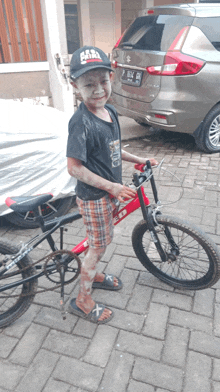 a young boy wearing a hat that says ' para mafia ' on it stands next to a bicycle