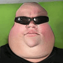 a fat man wearing sunglasses is sitting on a green couch .