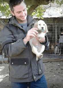 a man in a jacket holds a small white puppy in his arms