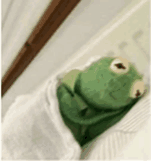 a kermit the frog stuffed animal is wrapped in a white blanket .