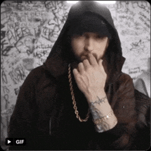 a man in a hooded jacket with a gold chain around his neck has a tattoo on his wrist