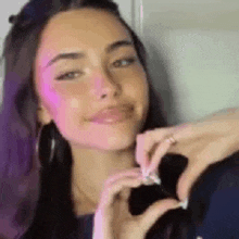 a woman is making a heart shape with her hands and smiling .